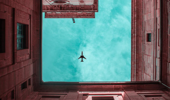 Surrounded by buildings while looking upward to an airplane in the sky