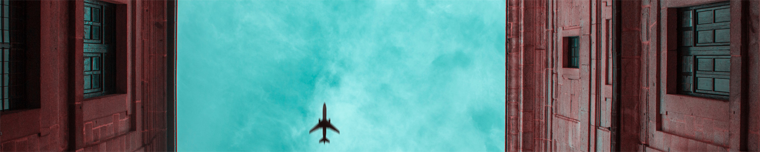 Plan flying above in a blue sky with buildings on the left and right
